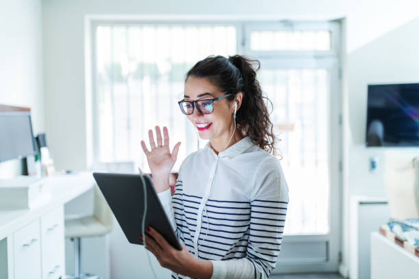 smiling beautiful caucasian businesswoman having video call over the tablet and waving while standing in modern office. - social housing audio imagens e fotografias de stock