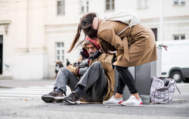 Young woman giving money to homeless beggar man sitting in city. A young woman giving money to homeless beggar man sitting outdoors in city. beggar stock pictures, royalty-free photos & images