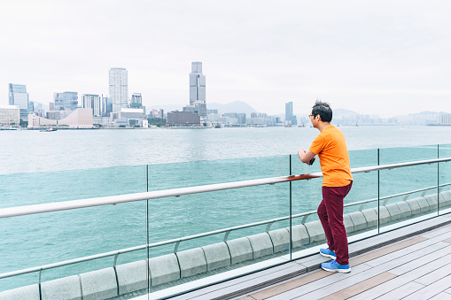 Man in his 50s in casual clothes, leaning on railing and looking at view, standing on decking, leisure, travel, solitude, contemplation