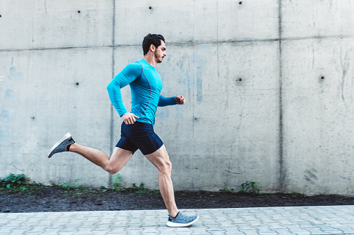 Side view of young man running outdoors in morning. Male athlete in running outfit sprinting outdoors.