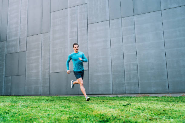 Side view of young man running outdoors in morning. Male athlete in running outfit sprinting outdoors.