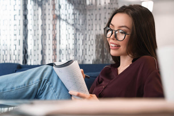 istock Cheerful young girl in glasses making notes in her notebook 1125046323