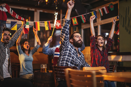 Group of young people, sitting in a pub all together, watching a sports game.