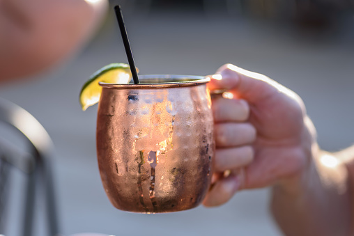 Hand holding up a bright copper mug of Moscow mule for celebration toast cheers