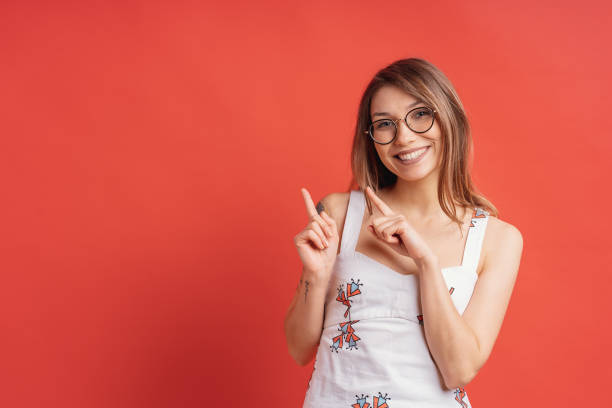 istock Smiling young female with glasses, pointing aside to red background 1125090725
