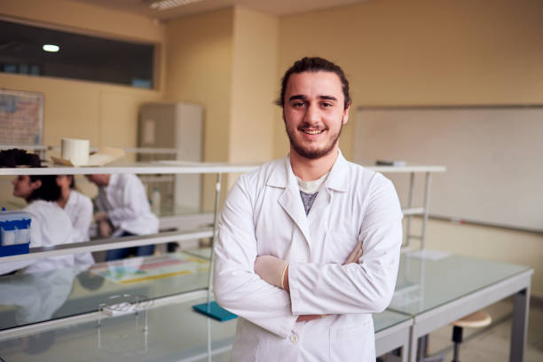 Male scientist looking at camera with a little smile in the lab. Young male genetics student in the laboratory with collegues stock photo