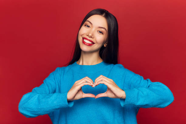 istock Studio portrait of pretty cute tender cheerful nice beautiful attractive charming she her girl making heart on chest isolated on red background 1125093361