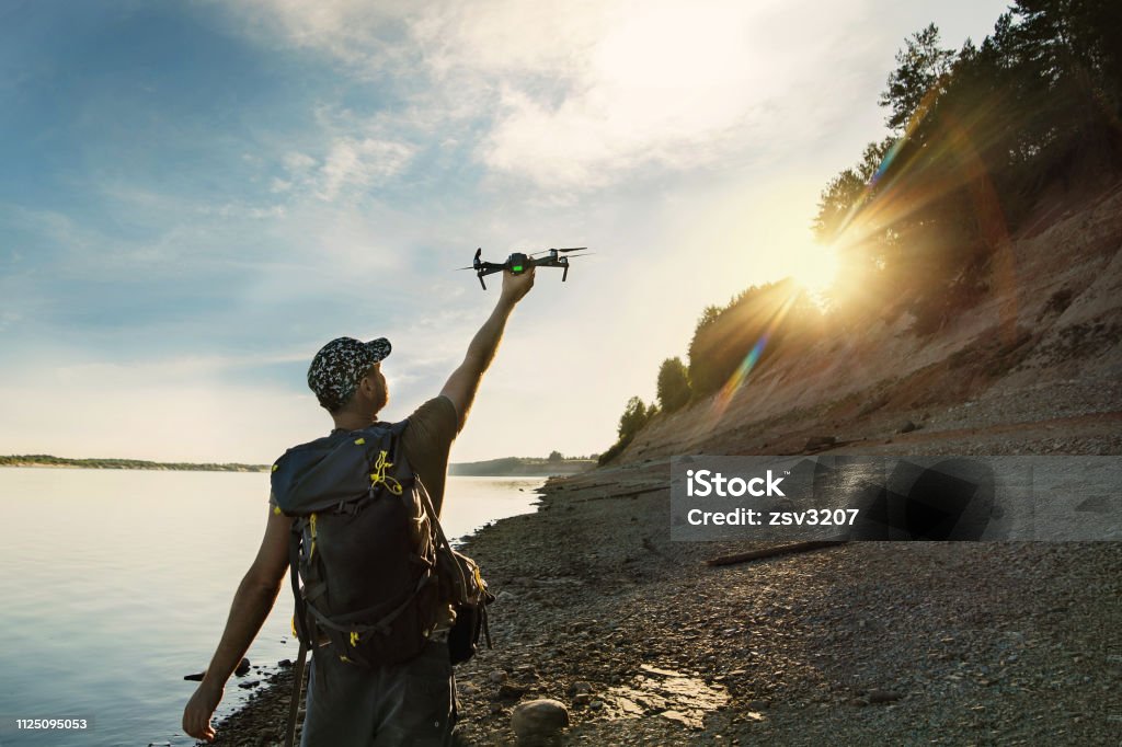 Male tourist launching drone from hand in beautiful sunset in woodland Male tourist launching drone from hand in beautiful sunset in woodland. Drone Stock Photo