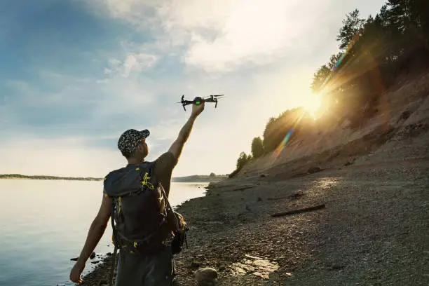Photo of Male tourist launching drone from hand in beautiful sunset in woodland