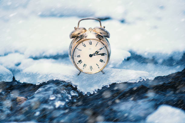 istock Frozen time. A clock on an ice next to the water. Extreme weather situation. Snow falling on a clock in a nature. Golden old clock. 1125106364