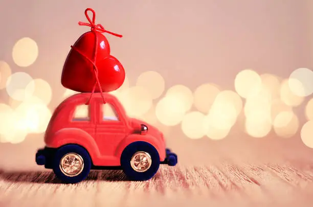 Photo of Little red beetle car carries a heart. The concept of Valentine Day.