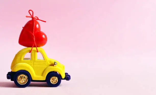 Photo of Little yellow beetle car carries a heart. The concept of Valentine Day.