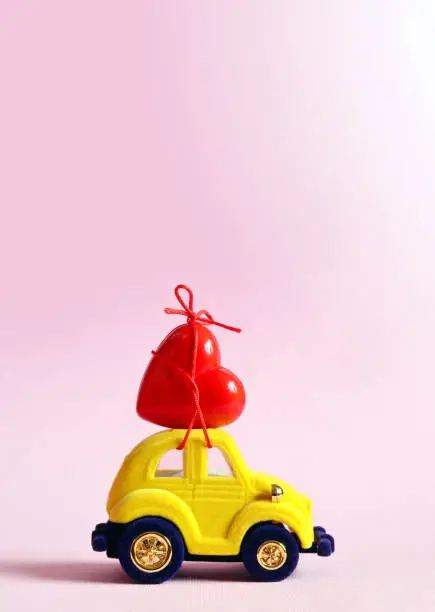 Photo of Little yellow beetle car carries a heart. The concept of Valentine Day.