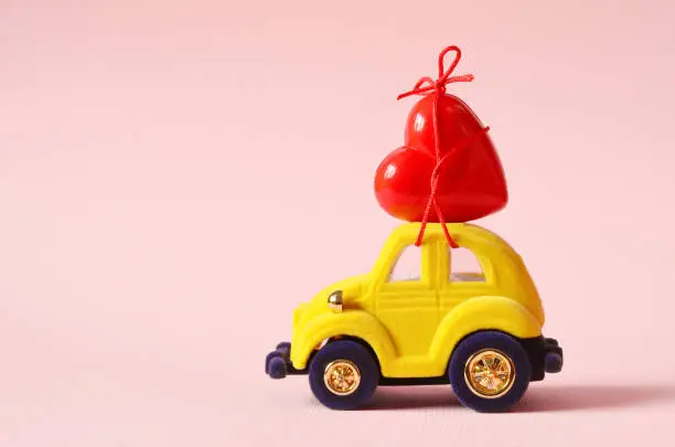 Photo of Little yellow beetle car carries a heart. The concept of Valentine Day.