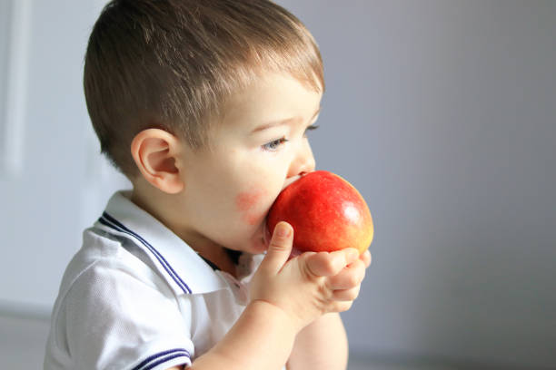 ritratto ravvicinato di un simpatico bambino con dermatite atopica sulla guancia che tiene e mangia mela rossa. allergia alimentare - cute little boys caucasian child foto e immagini stock