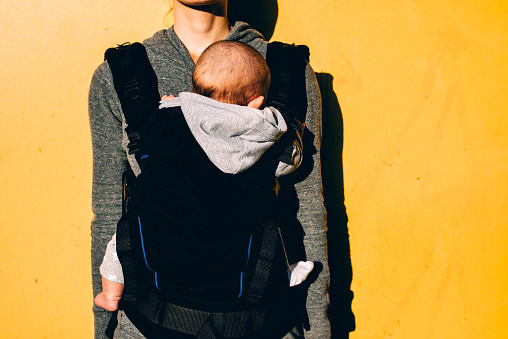 little baby in carrier and mother on yellow background attachment parenting