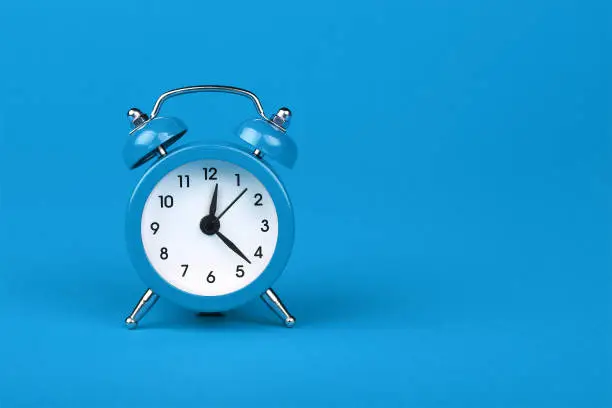 Photo of Close up one blue alarm clock over blue background