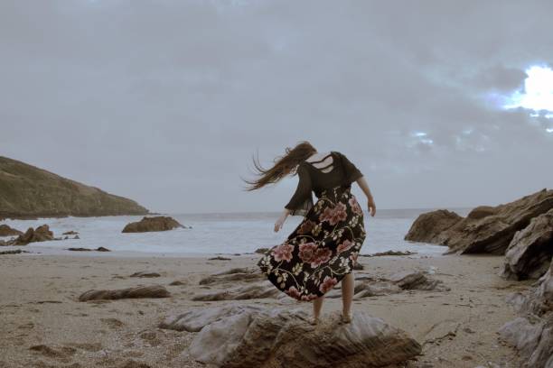 istock Lady in a formal floral patterned dress on a dramatic grey windy beach 1125182181