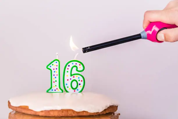 Photo of Man's hand lighting sixteenth birthday candles on rustic vanilla layer cake