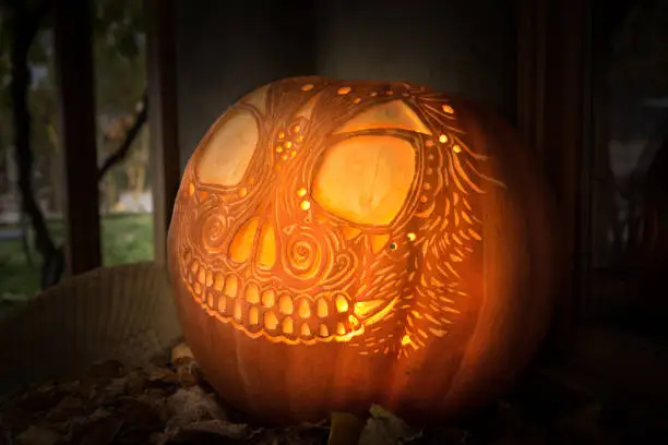 Photo of Artistically carved glowing jack-o'-lantern on tabletop display with leaves for Hallowe'en