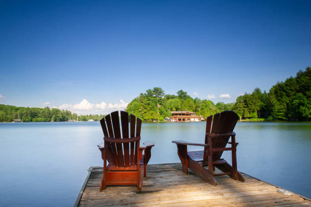 istock Two Adirondack chairs sit on a wooden dock facing a calm lake 1125219641