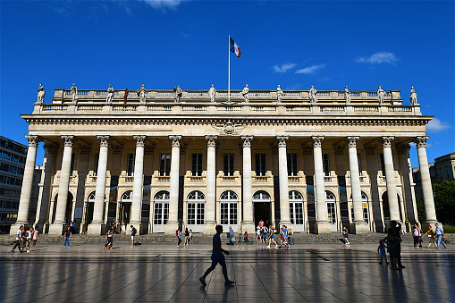 People walking in front of the neo-classical facade of The Grand Théâtre de Bordeaux, home to the Opéra National as well as the Ballet National de Bordeaux.