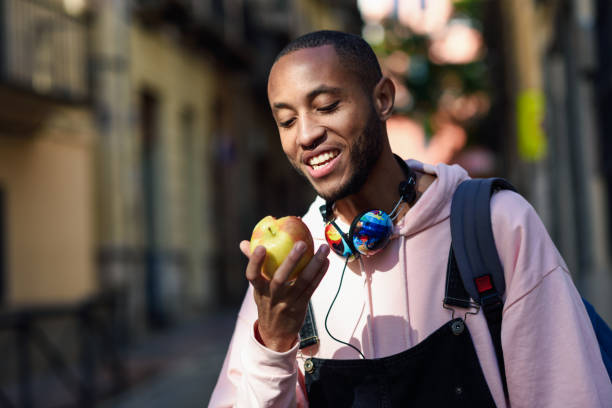 istock Young black man eating an apple walking down the street. 1125261083