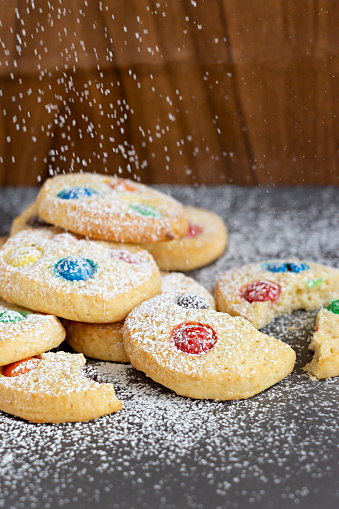 Homemade shortbread cookies with multicolored chocolate chips and icing powdered on gray background. Selective focus. Christmas concept. Copy space.