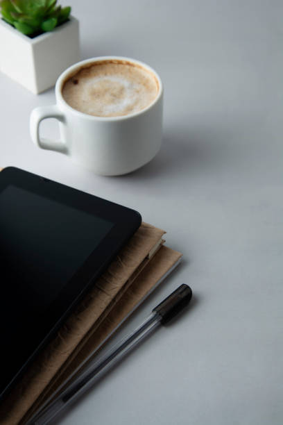 istock Work table with coffee cup, notepad screen and notebook. Education and business concept. Grey background, minimalistic style. Vertical image. 1125306459