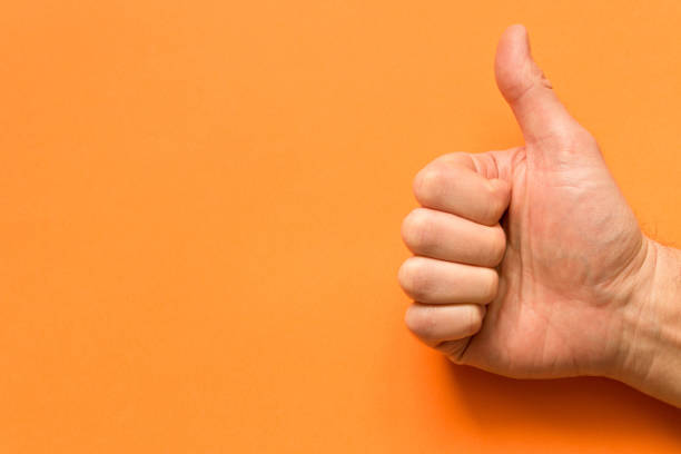 istock The hand of a man with his thumb up. On an orange background. Empty text space. 1125315247