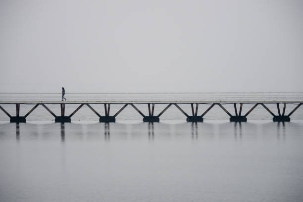 Lonely man walking on a bridge over water in Lisbon, foggy atmosphere, copyspace