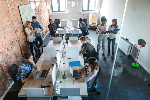 High angle view of large group of multi-tasking entrepreneurs working at corporate office. The view is through glass.