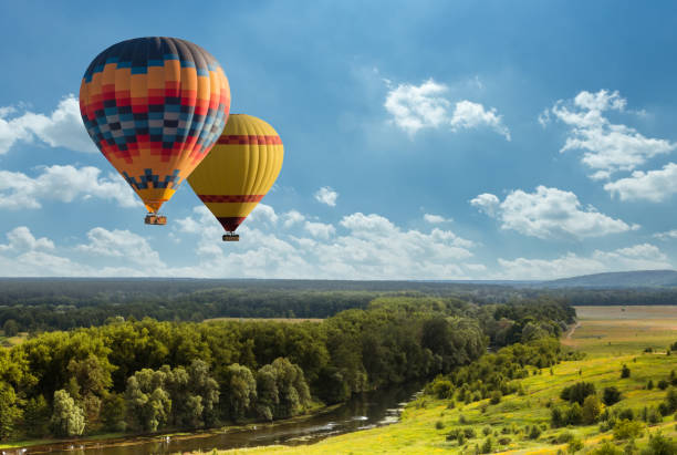 colorido globo aerostático volando sobre el campo verde - globo aerostático fotografías e imágenes de stock