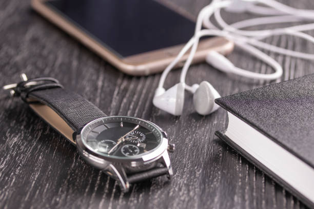 Wrist watch, mobile phone with headphones and notepad on an old dark office desktop