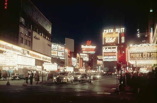 New York City, NY, USA, 1955. Times Square at night. Furthermore: cinemas, theaters, traffic, restaurant, neon signs, lighting, curious people, visitors, billboards and buildings.