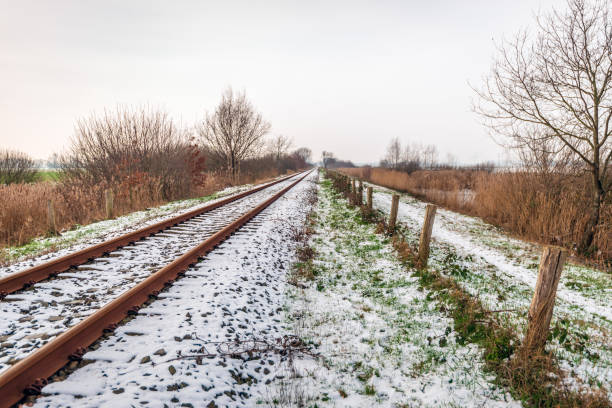 Single-track rails in a Dutch winter landscape covered with a layer of snow. Beside the rails is a fence made of wooden posts and barbed wire.