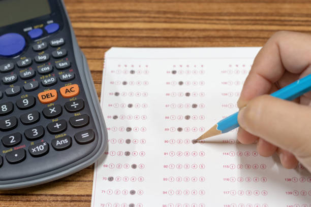 Dry hand of mature student doing exams by using pencil selected multiple choice on standardized test form with answers bubble with calculator nearby. Ideas about adult education and life long learning mano seca de alumna madurita haciendo exámenes usando el lápiz había seleccionado opción múltiple en forma de prueba estandarizada con la burbuja de respuestas con la calculadora cerca. ideas sobre educación de adultos y aprendizaje a lo largo de la