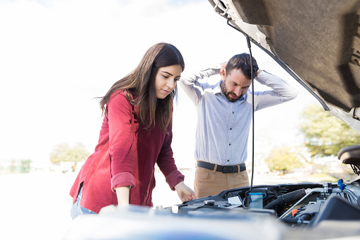 Multiethnic couple standing near breakdown car during road trip