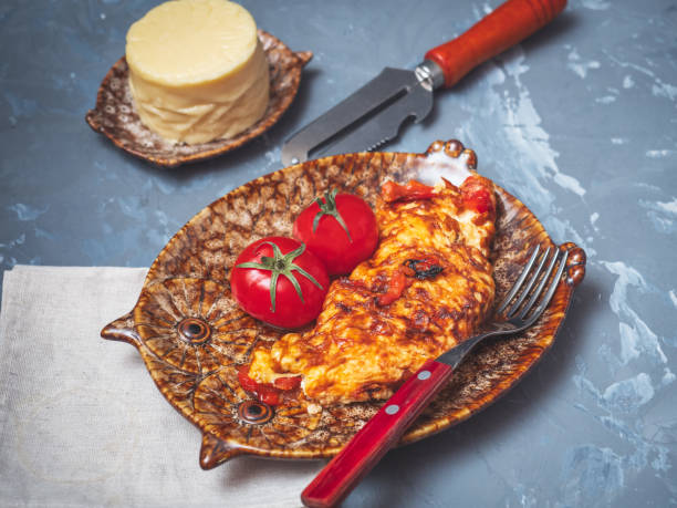Freshly cooked omelet with vegetables and cheese on a decorative plate with fresh red tomatoes.