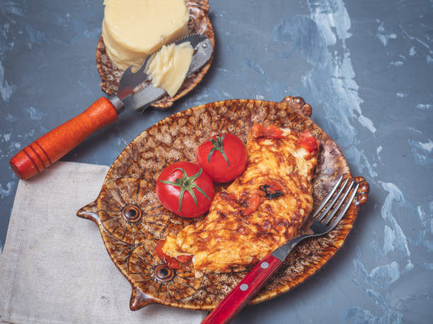 Omelette with vegetables and cheese on a decorative plate and two whole red tomatoes with leaves.