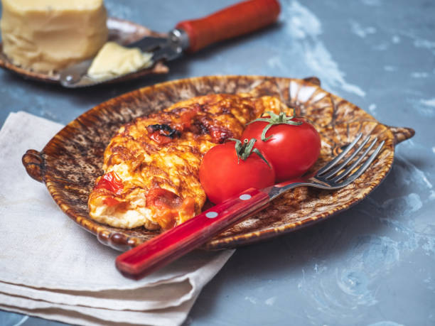 Omelette with vegetables and cheese with whole tomatoes. Fork and cheese knife with wooden handles.