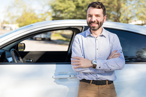 Smiling mid adult man making eye contact while standing arms crossed near white car