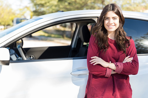 Portrait of pretty Caucasian woman standing arms crossed against new white car on sunny day