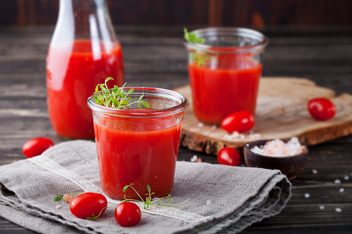 Tomato juice in glass with cress salad, fresh tomatoes on wooden cutting board and grey towel