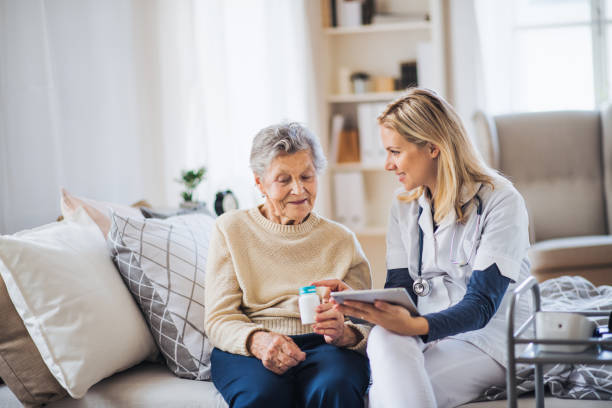 A health visitor with tablet explaining a senior woman how to take pills. A young health visitor with tablet explaining a senior woman how to take medicine and pills. senior home stock pictures, royalty-free photos & images