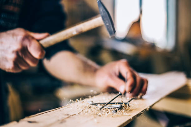 Close up of man hammering a nail into wooden board stock photo