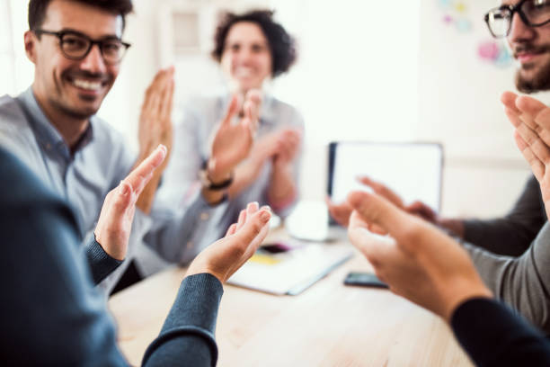 istock Group of young businesspeople sitting around table in a modern office, clapping. 1125366439
