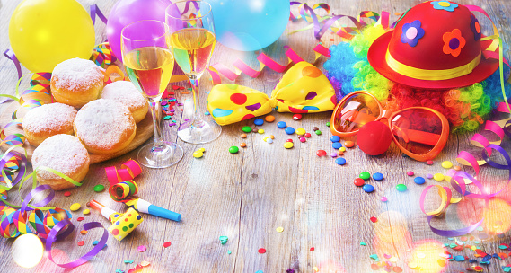 Colorful carnival or party background with donuts, balloons, streamers and confetti and funny face formed from wig, nose and glasses on rustic wooden planks with copy space