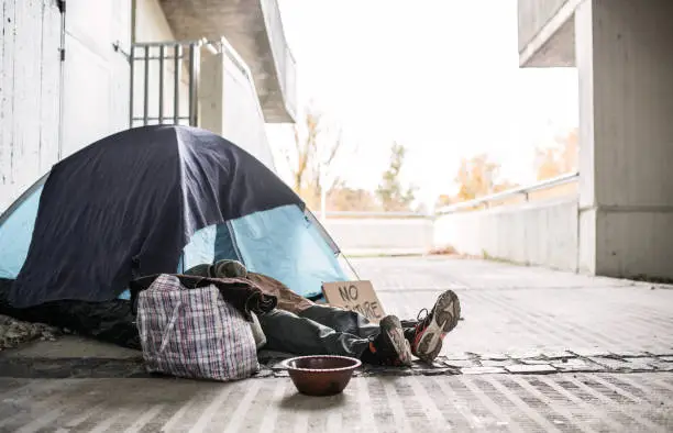 Photo of Legs and feet of homeless beggar man lying on the ground in city, sleeping in tent.