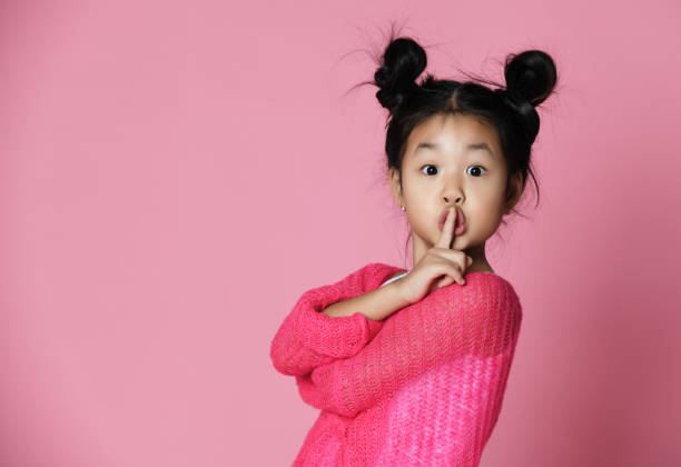 Asian kid girl in pink sweater shows shh sign Close up portrait stock photo
